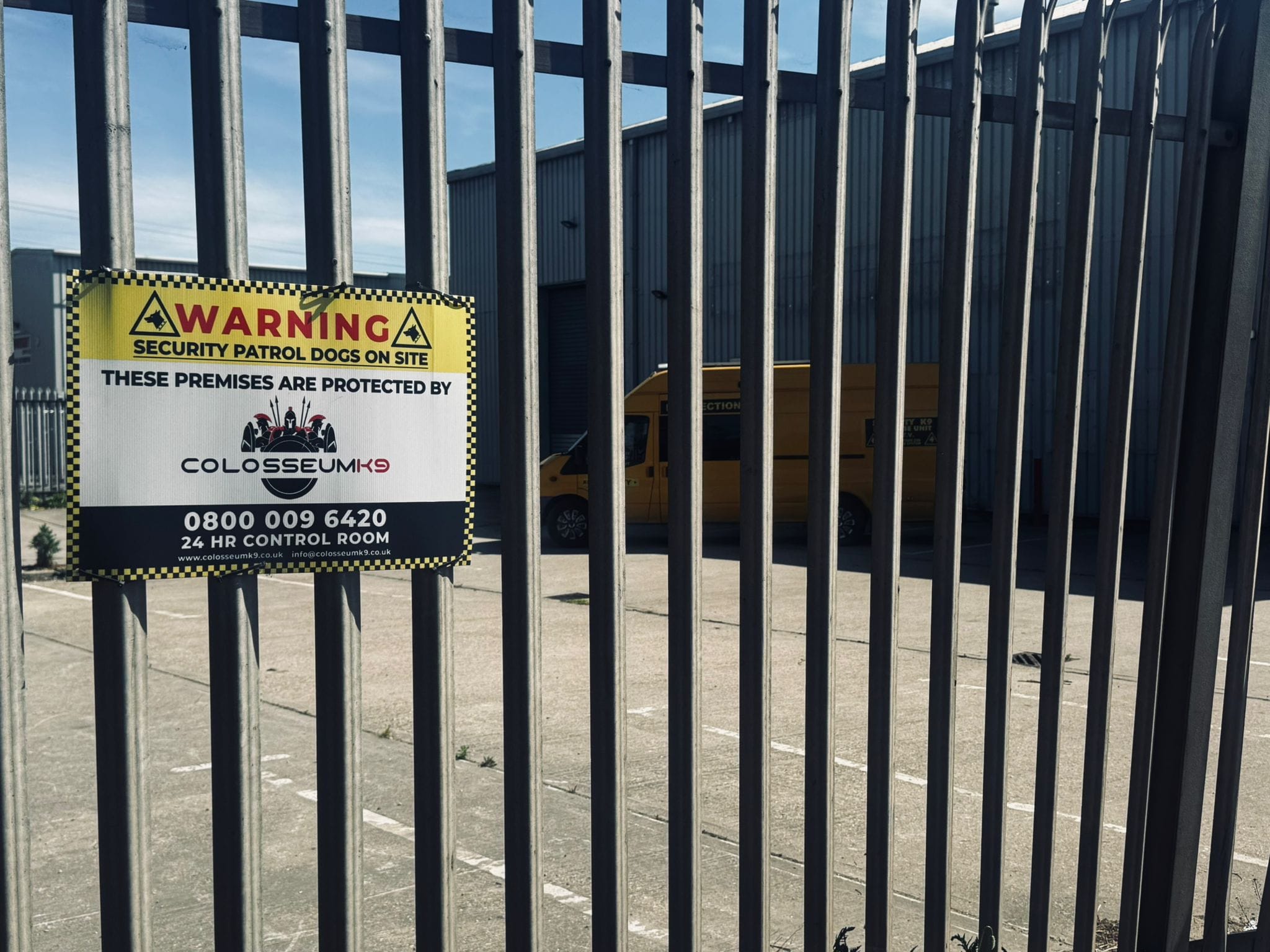 Security dog handler cost guide showing a Colosseum K9 patrol dog warning sign on an industrial site perimeter.