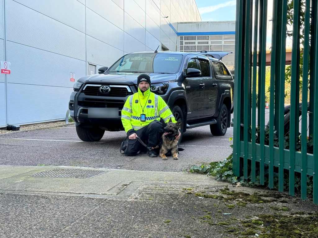 Security dog handler and trained dog beside a patrol vehicle at a commercial site